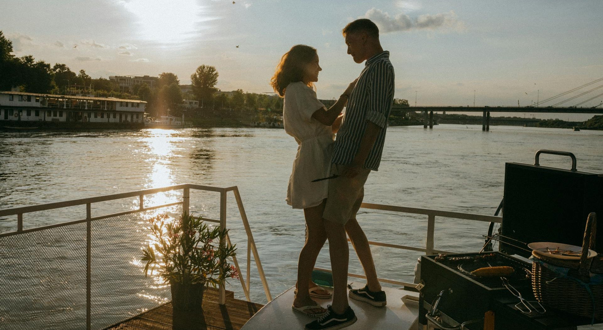 Couple standing on a boat deck by a river at sunset